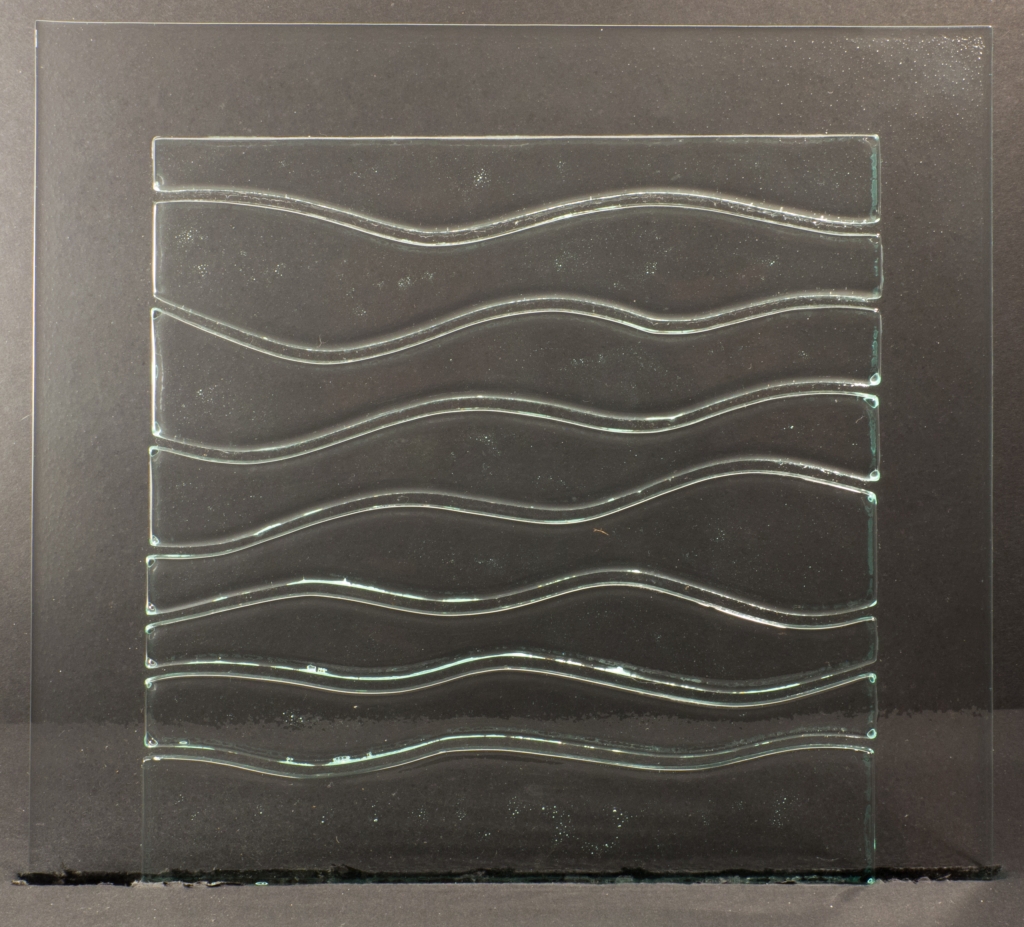 A square glass panel with an inset area, also square. The inset area is broken up with a series of curved lines, forming a wavelike pattern.
